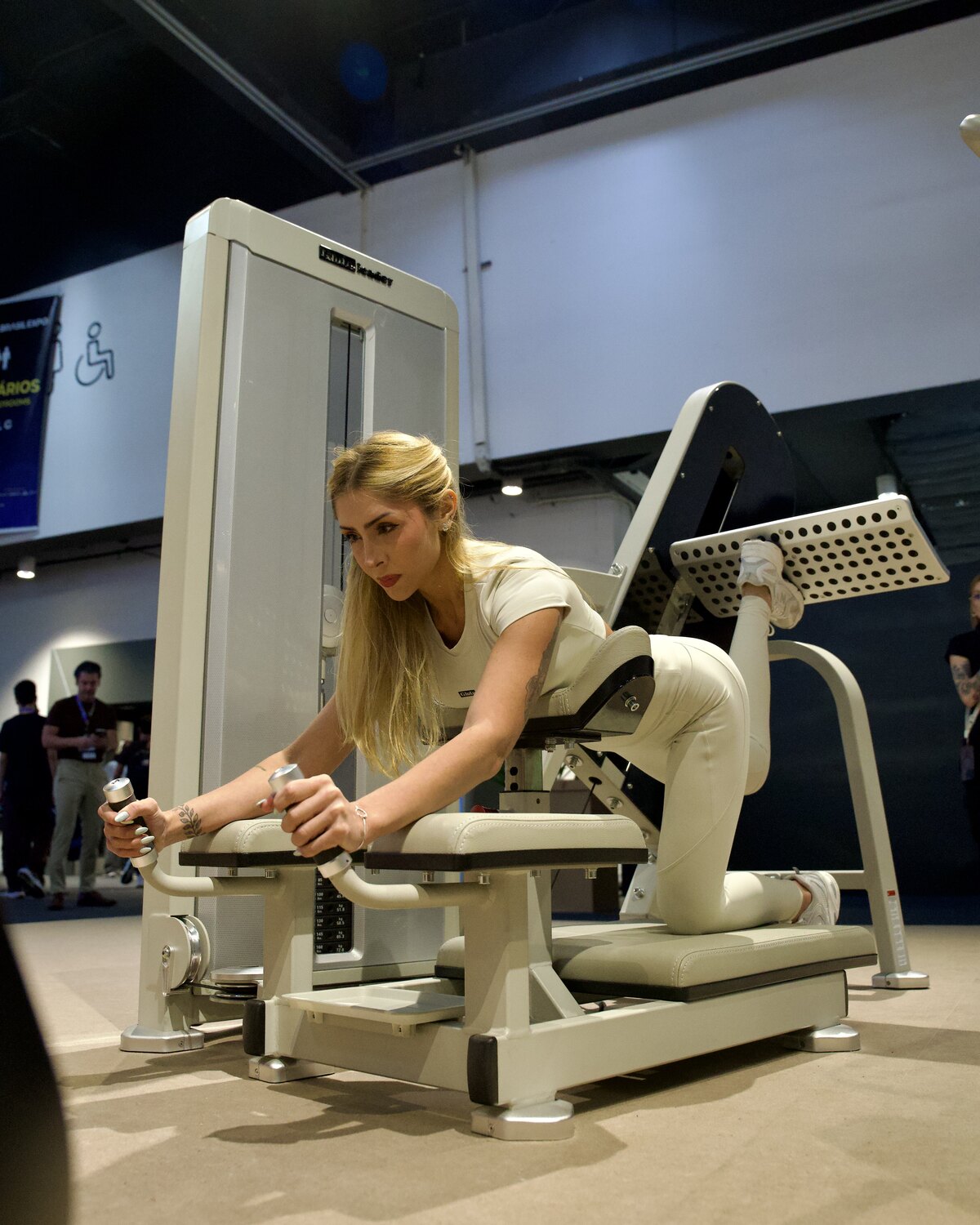 Woman demonstrating a kneeling kickback movement on a GluteLeader machine at a fitness exhibition